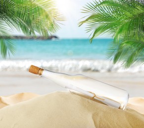 Corked glass bottle with rolled paper note on sandy beach with palms near ocean