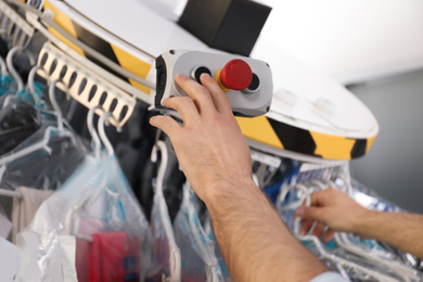 Worker pressing button on control panel of garment conveyor at modern dry-cleaner's, closeup