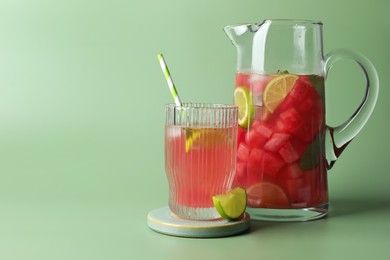Tasty summer watermelon drink with lime in jug and glass on pale light green background. Space for text