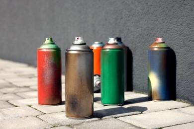 Cans of different spray paints on pavement near wall