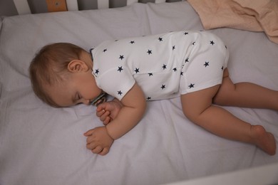 Adorable little baby with pacifier sleeping in crib, above view