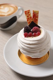 Delicious meringue dessert with berries and cup of coffee on wooden table, closeup