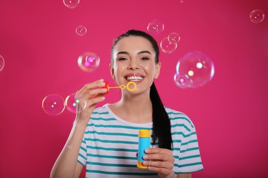 Photo of Young woman blowing soap bubbles on pink background