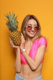 Young woman with fresh pineapple on yellow background. Exotic fruit