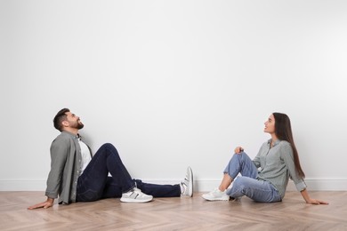 Young couple sitting on floor near white wall indoors. Space for text