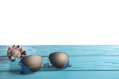 Stylish sunglasses and shell on light blue wooden table against white background. Space for text