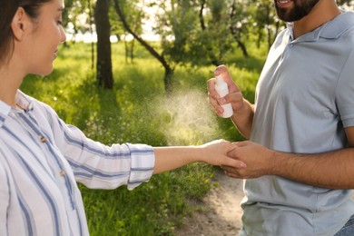 Man applying insect repellent on his girlfriend's arm in park, closeup. Tick bites prevention