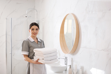 Young chambermaid holding stack of fresh towels in bathroom