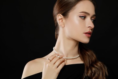 Young woman wearing elegant pearl jewelry on black background, space for text