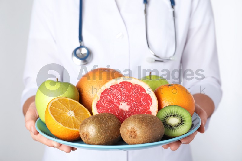 Female nutritionist with fruits on light background, closeup