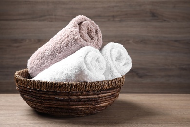 Rolled soft towels in wicker basket on wooden table. Space for text