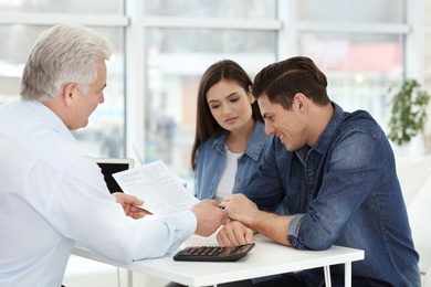 Young couple discussing pension plan with mature consultant in office