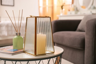 Stylish holder with burning candle and reed air freshener on table in room