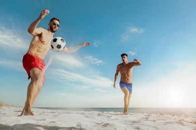 Image of Friends playing football on beach during sunny day, low angle view
