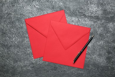 Red envelopes and pen on grey table, top view