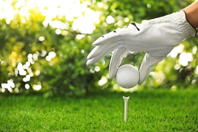 Player putting golf ball on tee at green course, closeup