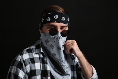 Fashionable young man with bandana covering his face on black background