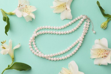 Photo of Flat lay composition with elegant pearl necklace and beautiful flowers on turquoise background