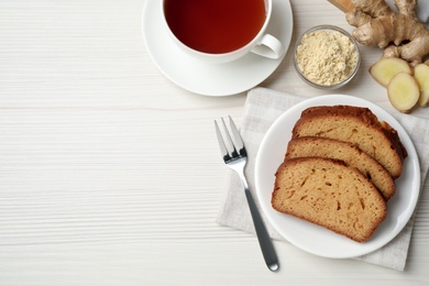 Slices of delicious gingerbread cake served with tea on white wooden table, flat lay. Space for text