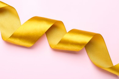 Beautiful golden ribbon on pink background, top view