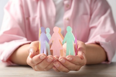 Photo of Woman holding paper human figures at table, closeup. Diversity and inclusion concept