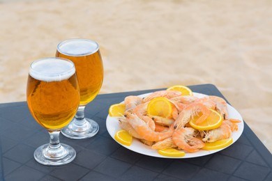 Photo of Cold beer in glasses and shrimps served with lemon on beach