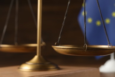 Scales of justice and European Union flag on wooden table, closeup
