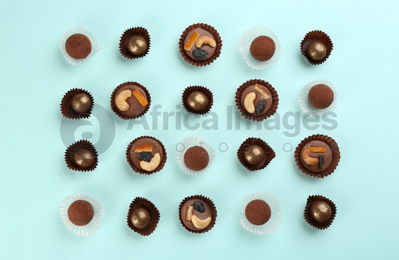 Photo of Different delicious chocolate candies on light blue background, flat lay