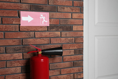 Fire extinguisher and emergency exit sign on brick wall indoors