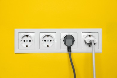 Power sockets with inserted plugs on yellow wall. Electrical supply