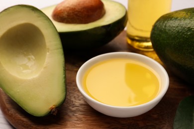 Photo of Cooking oil in bowl and fresh avocados on wooden table, closeup