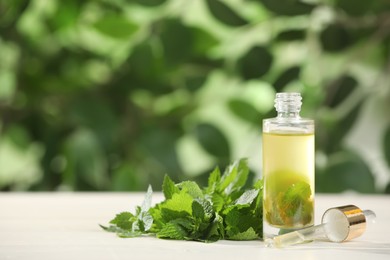 Glass bottle of nettle oil with dropper and leaves on white table against blurred background, space for text