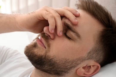 Young man suffering from migraine in bed, closeup
