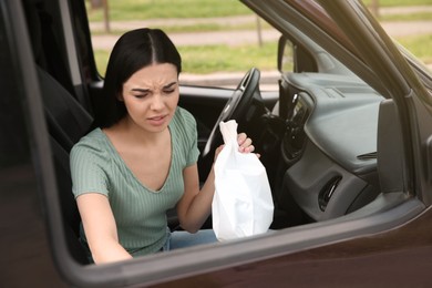 Young woman with paper bag suffering from nausea in car