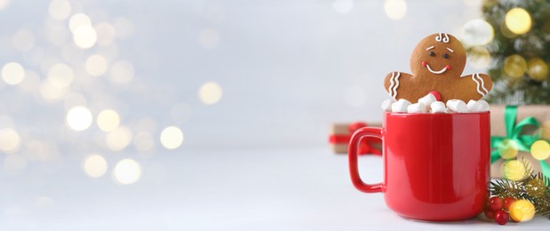 Image of Gingerbread man in red cup with marshmallows on white table, space for text. Banner design