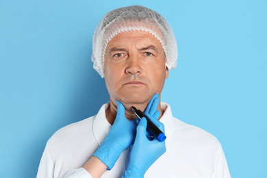 Surgeon with marker preparing man for operation against blue background. Double chin removal