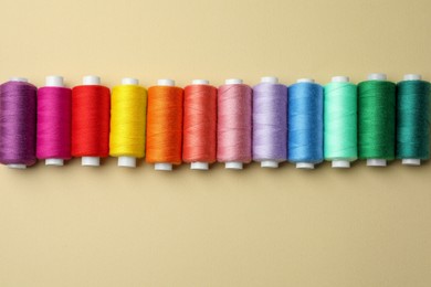 Set of colorful sewing threads on beige background, flat lay. Space for text