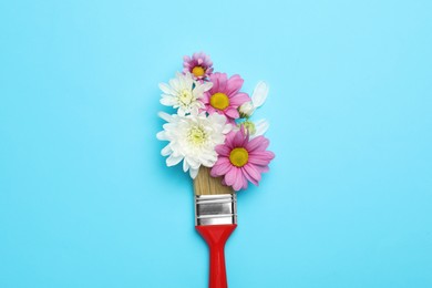 Photo of Brush painting with chrysanthemum flowers on light blue background, top view. Creative concept