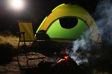 Smoking bonfire and folding chairs near camping tent outdoors at night