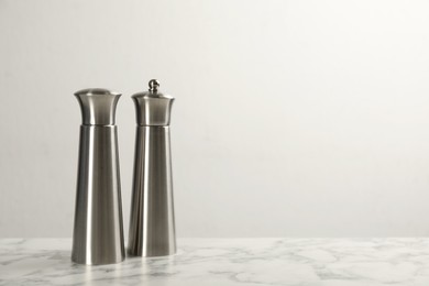 Stainless salt and pepper shakers on marble table against white background. Space for text