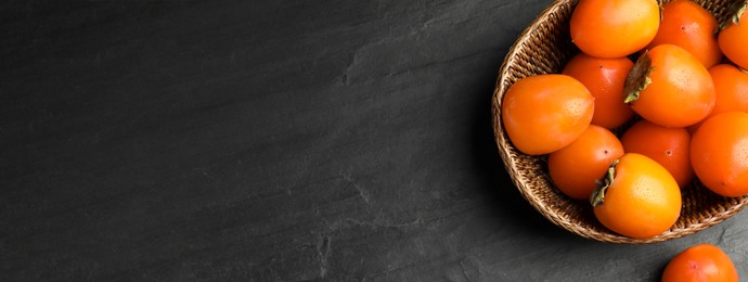 Delicious fresh persimmons on black slate table, top view with space for text. Banner design