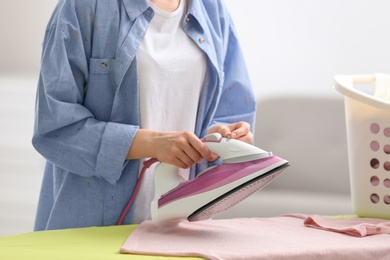 Photo of Young woman ironing clean laundry on board indoors, closeup