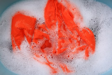 Orange garment in suds, top view. Hand washing laundry