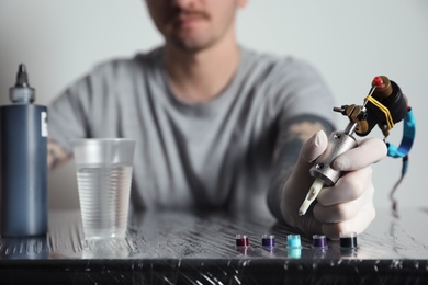 Photo of Tattoo artist with machine and ink at table, closeup