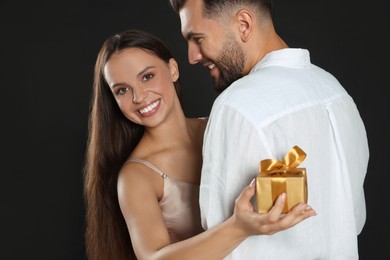 Photo of Woman presenting gift to her boyfriend on black background