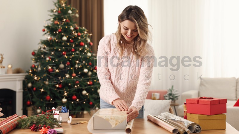 Beautiful young woman wrapping Christmas gift at home