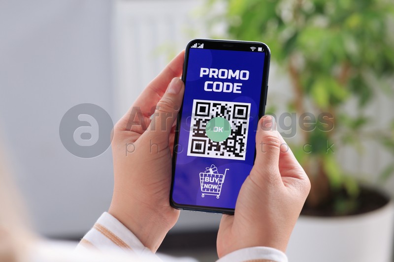 Photo of Woman holding smartphone with activated promo code in online shopping app indoors, closeup