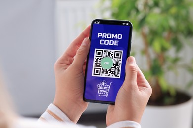 Photo of Woman holding smartphone with activated promo code in online shopping app indoors, closeup