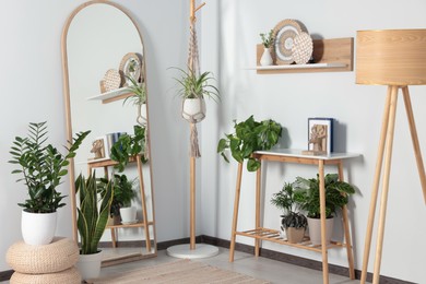 Photo of Stylish room interior with wooden furniture, houseplants and full length mirror near white wall