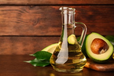Photo of Glass jug of cooking oil and fresh avocados on wooden table, space for text